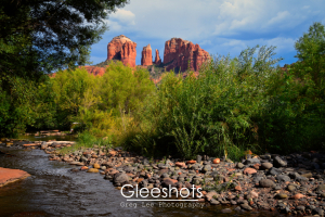 In this scene from Sedona, the red rock formations of Cathedral Rock tower over a creek with rounded stones and lush green vegetation.  Arizona Fine Art Landscape Photography Print for Sale.