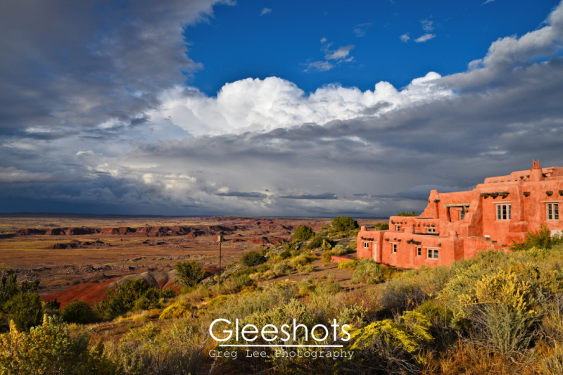 The coral pink adobe-style Painted Desert Inn glows at sunset,  with dramatic clouds overhead and a desert landscape stretching into the distance at Petrified Forest National Park.  Arizona Fine Art Landscape Photography Print for Sale.