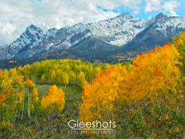 Seasons clash in this scene of the San Juan Mountains, as vibrant autumn foliage, with yellow and orange aspen trees, lead to majestic snow-capped mountains in the background.  Colorado Fine Art Landscape Photography Print for Sale.