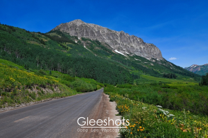The road to Gothic Colorado leads through green meadows and wildflowers towards Gothic Mountain. The mountain rises prominently in the background with patches of snow.  Colorado Fine Art Landscape Photography for Sale.