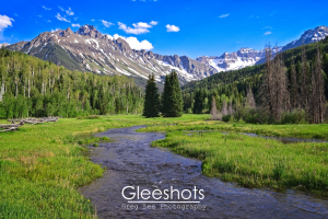 A clear mountain stream winds through a lush green meadow surrounded by trees, with the snow-capped peaks of Mt Sneffels in the background.  Colorado Fine Art Landscape Photography Print for Sale.