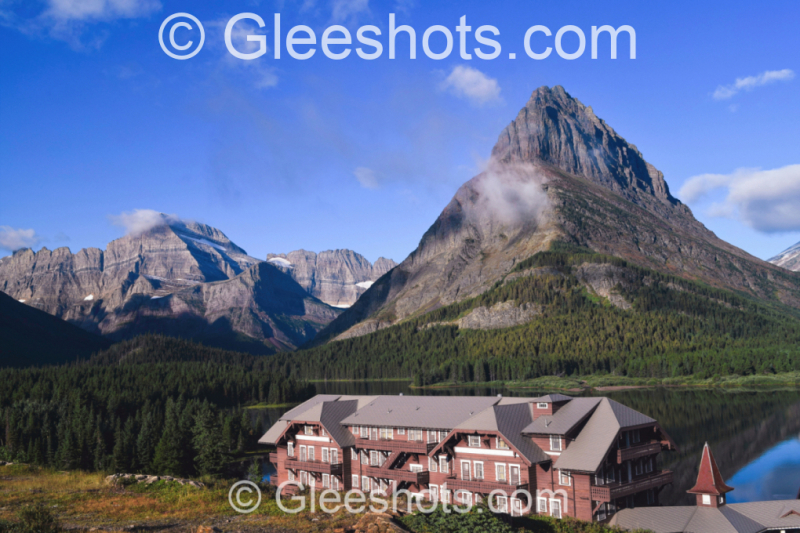 The historic Many Glacier Hotel and Swiftcurrent Lake in Glacier National Park, with light wispy clouds among a clear blue sky.   Montana Fine Art Landscape Photography Print for Sale.