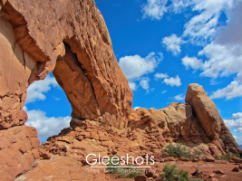 A view of the North Window arch in Arches National Park under a blue sky filled with puffy clouds.  Utah Fine Art Landscape Photography for Sale.