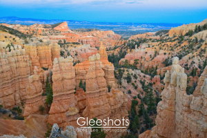 A view of Bryce Canyon at sunset from Fairyland Point, showing a pastel palette of orange, yellow, and pink hoodoos and rock formation, with distant mesas in the background.  Utah Landscape Photography Print for Sale.