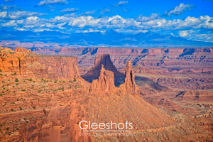 At the Mesa Arch Overlook in Canyonlands National Park, sunlight and shadows highlight the red rock formations in the canyon below, with the snow-capped La Sal Mountains in the distance.  Utah Fine Art Landscape Photography Print for Sale.