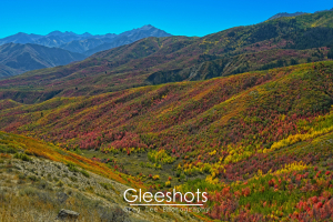 At the Deer Creek Overlook, a scenic mountain landscape is shown with rolling hills covered in vibrant fall foliage in shades of red, yellow, and green under a clear blue sky.  Utah Fine Art Landscape Photography for Sale.