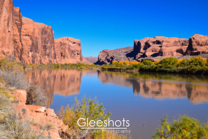 The Colorado River reflects red rock cliffs and the blue sky, with green and yellow fall foliage along the shore in Moab.  Utah Fine Art Landscape Photography Print for Sale.