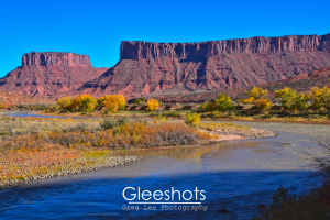 In Moab, the Colorado River curves through a landscape of autumn trees and shrubs, with dramatic red rock mesas rising in the background.  Utah Fine Art Landscape Photography for Sale.