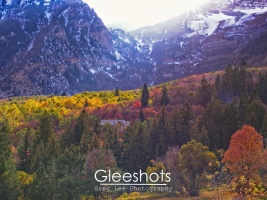 The setting sun shines down on a colorful mountain valley in autumn. highlighting the yellow and red foliage.  The snow-capped peaks of Mt Timpanogos are in the background, while a house can be seen nestled among the trees.  Utah Fine Art Landscape Photography for Sale.
