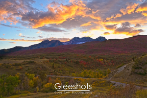A vibrant sunset sky glows over snow-capped Mt Timpanogos and rolling hills dotted with colorful autumn trees in shades of red, yellow, and green.   Utah Fine Art Landscape Photography for Sale.
